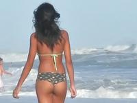 Charming bronze chick is sexily waving her bikini booty when walking in the sea waves